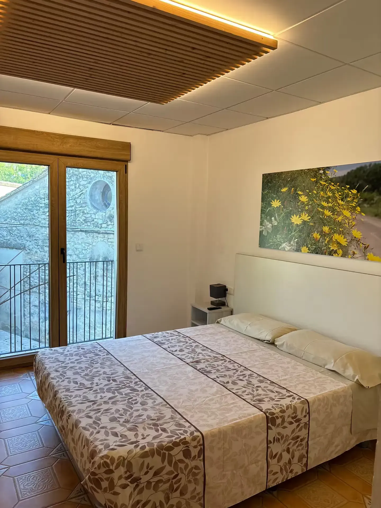 Dormitorio con cama doble, acceso al balcón, edredón con estampado floral, obras de arte y lámpara de techo texturizada.