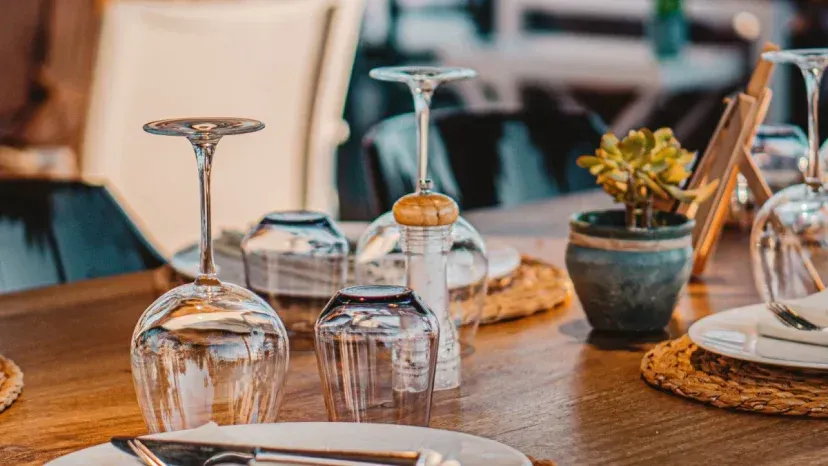 Mesa con copas de vino invertidas, platos y pequeña planta en maceta.