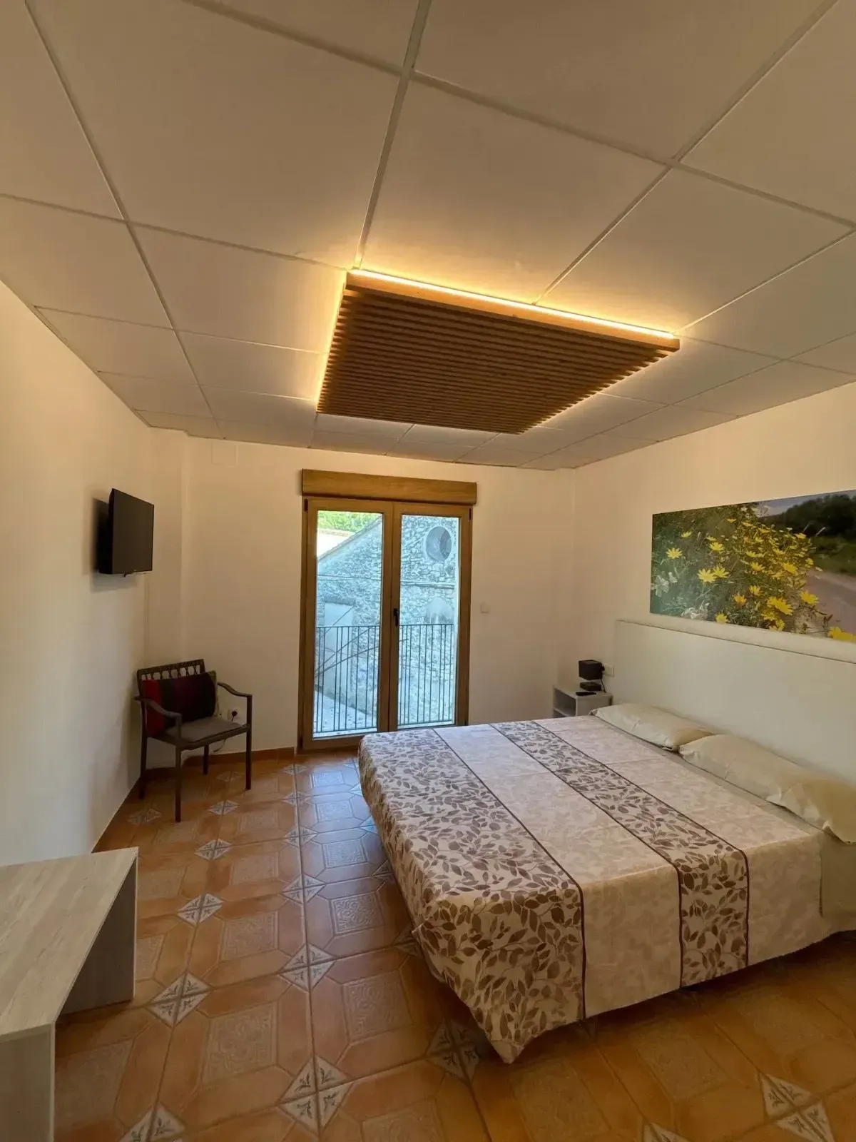 Dormitorio con cama doble, puertas de balcón, obras de arte y lámpara de techo estampada.