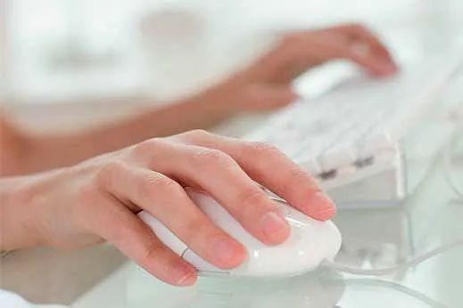 Una persona está escribiendo en un teclado de computadora mientras sostiene un mouse blanco.