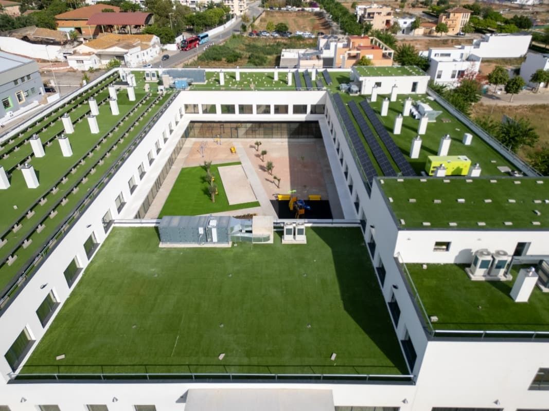 Vista aérea de un edificio escolar con techos verdes y un patio interior con zona de juegos.