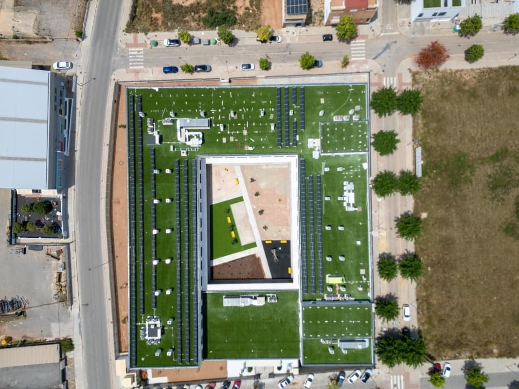 Vista aérea de un edificio moderno con techo verde, rodeado de calles, árboles y otras estructuras.