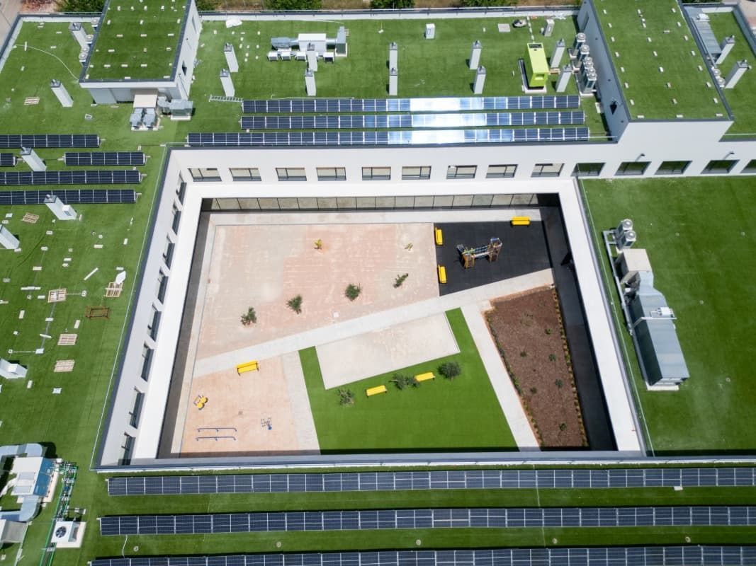 Vista aérea de un edificio con patio central. El edificio cuenta con paneles solares y techo verde. El patio cuenta con un área de juegos infantiles.