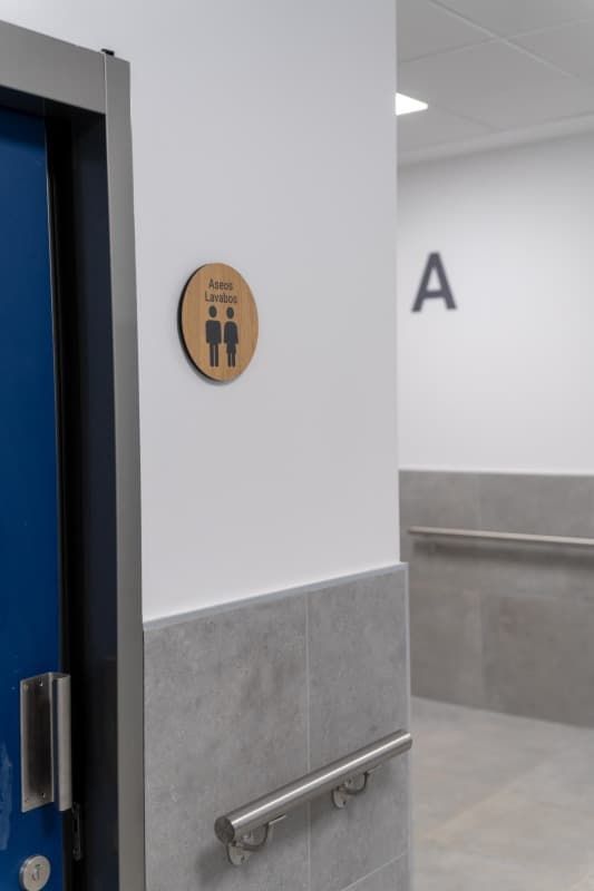 Un cartel de baño con figuras de palitos sobre un círculo de madera, con puerta y pasillo azules.