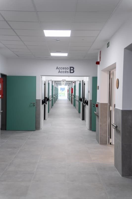 Pasillo del hospital con puertas color verde azulado, piso y paredes grises y un cartel que indica el acceso B.