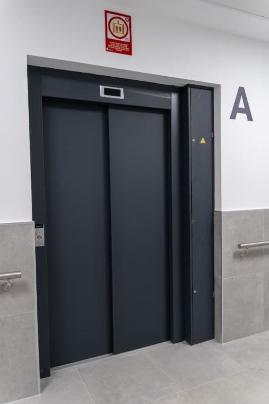 Ascensor gris oscuro con las puertas cerradas, al lado de una pared rotulada