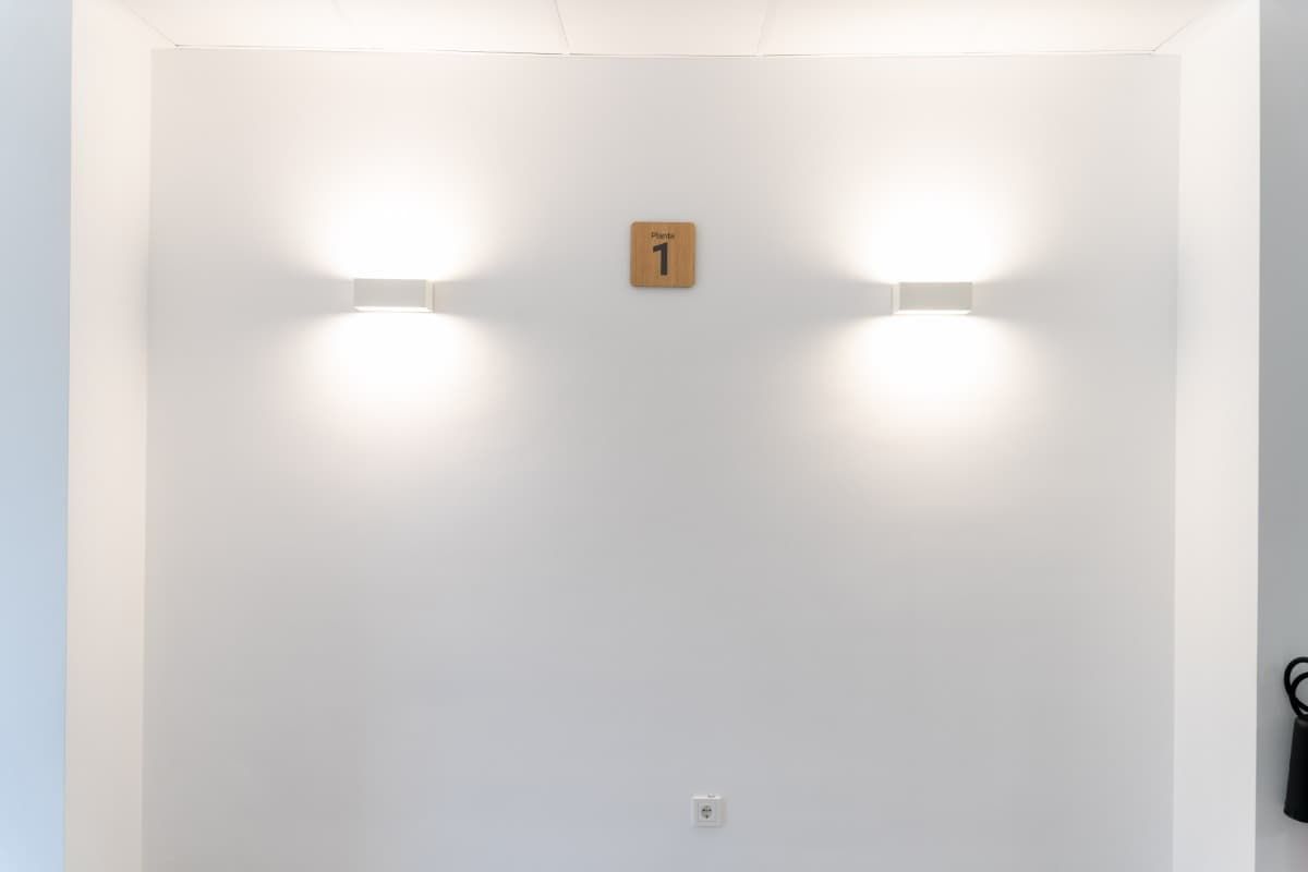 Pared blanca con dos apliques y cartel con el número 1.
