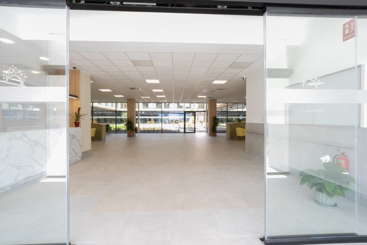 Vestíbulo vacío y moderno con puertas corredizas de vidrio, paredes blancas y piso de baldosas.