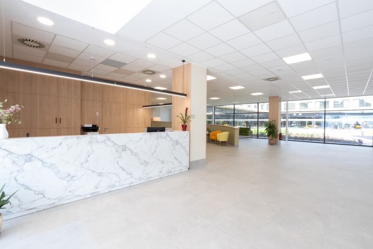 Área de recepción con mostrador de mármol, paneles de madera clara y grandes ventanales.