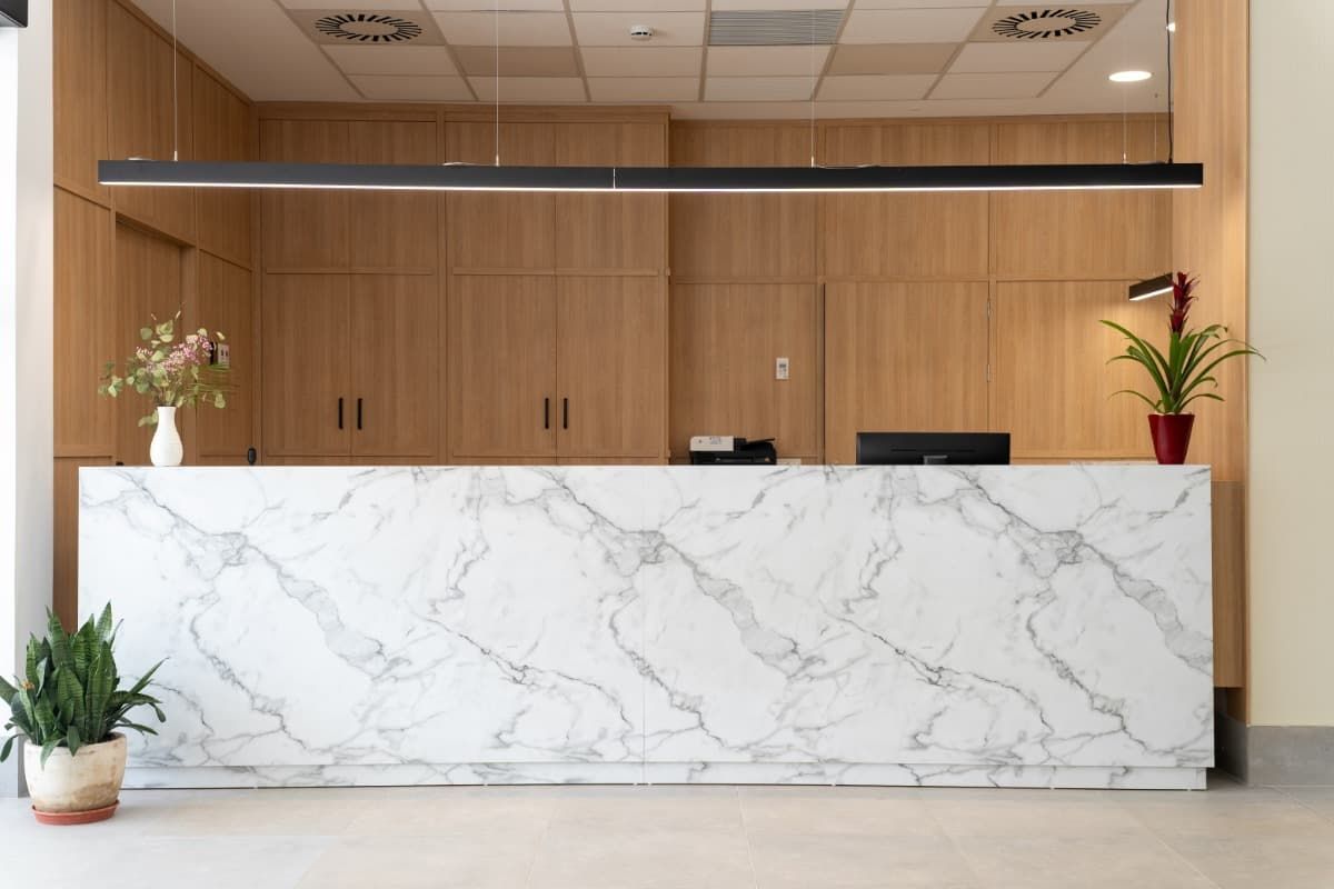 Mostrador de recepción con diseño de mármol, paneles de madera y plantas.