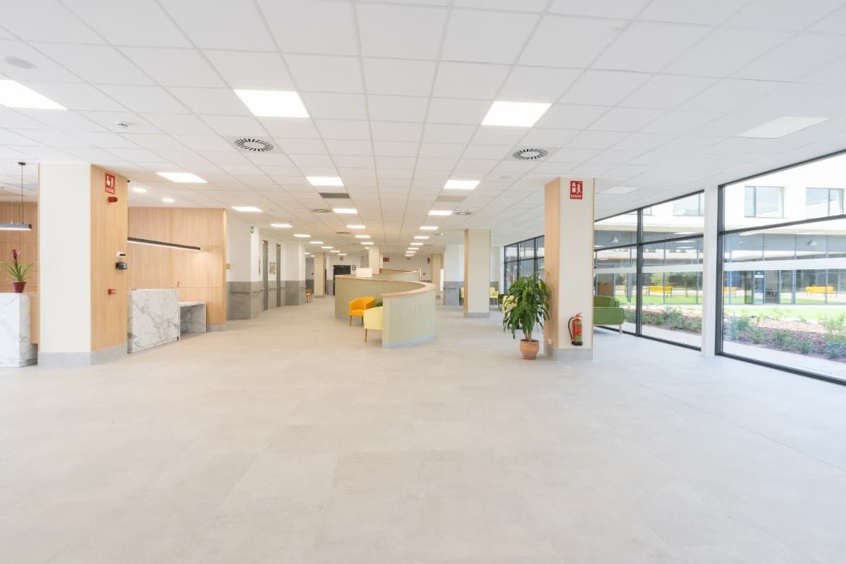 Interior espacioso y luminoso con grandes ventanales, colores neutros y cubículos.