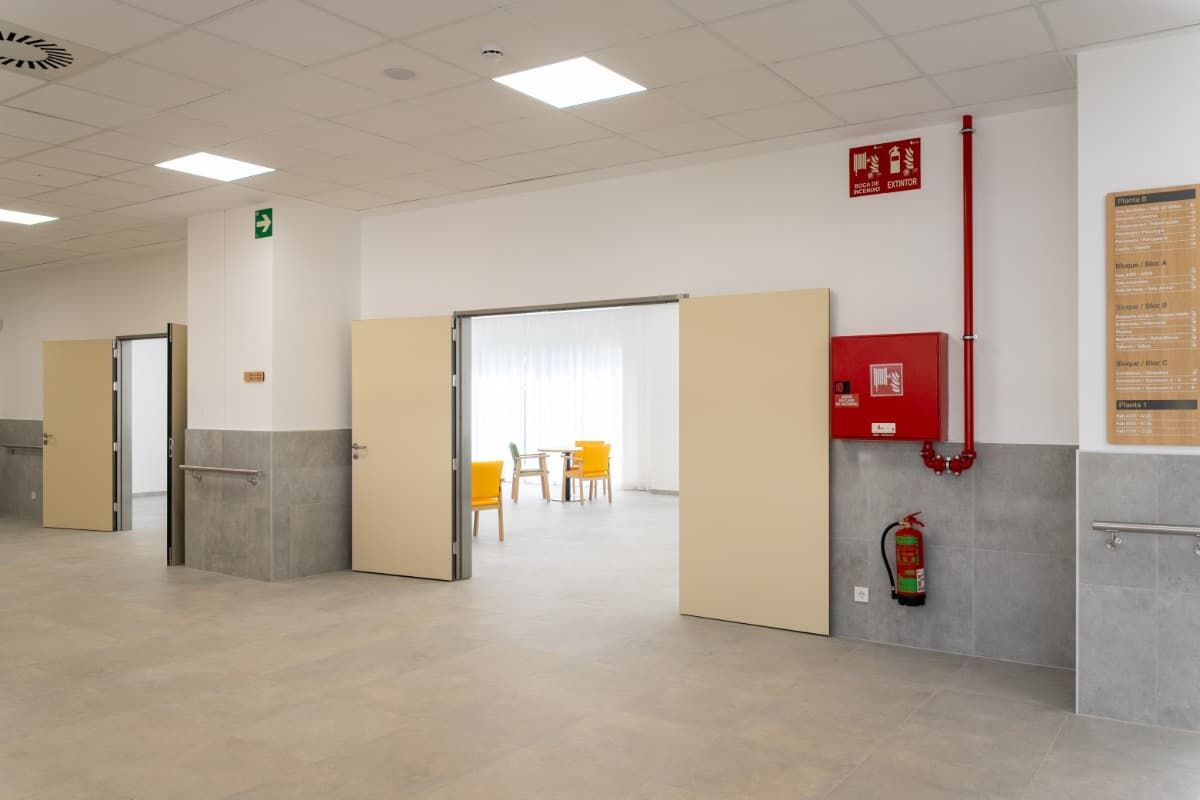 Pasillo interior con puertas beige, equipo de seguridad contra incendios y un vistazo a una zona de estar.