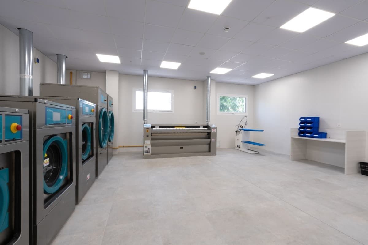 Lavandería con lavadoras, prensa y tabla de planchar.