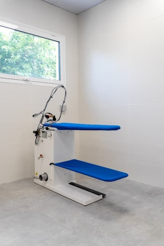 Máquina de planchar blanca y azul en una habitación vacía con ventana.