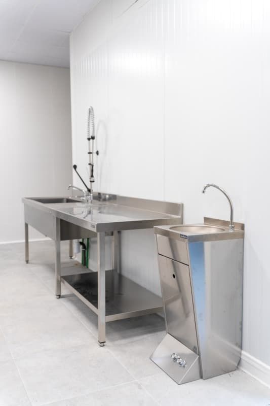 Fregadero de laboratorio de acero inoxidable y estación de lavado de manos en una habitación blanca.