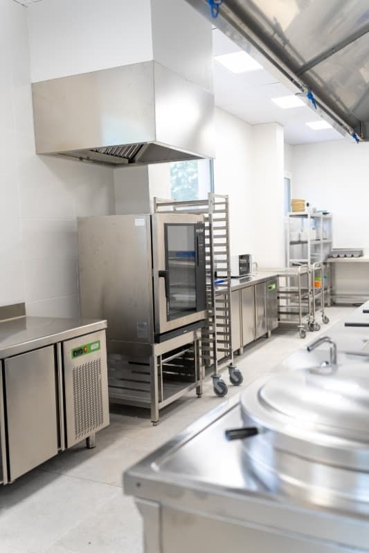 Cocina comercial de acero inoxidable, con horno con puerta abierta, campana extractora y encimeras.