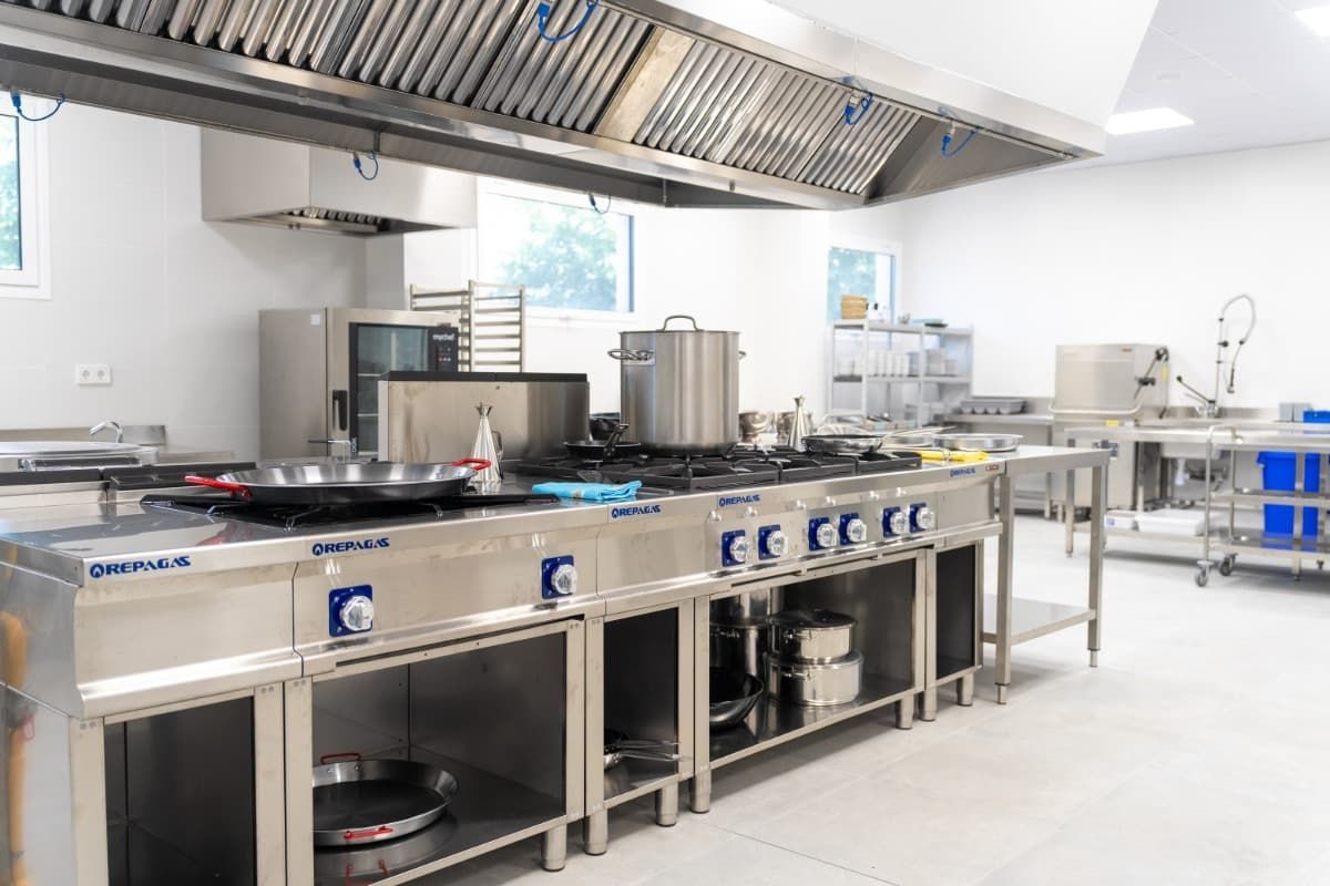 Cocina comercial de acero inoxidable con anafe, campana extractora y equipamiento.