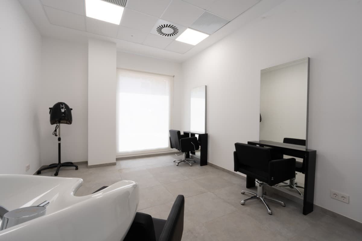 Interior de peluquería con paredes blancas, espejos, sillas y lavabo.