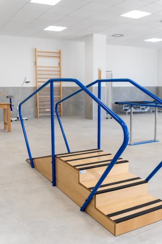 Escaleras de rehabilitación de madera con pasamanos azules en una sala de terapia.