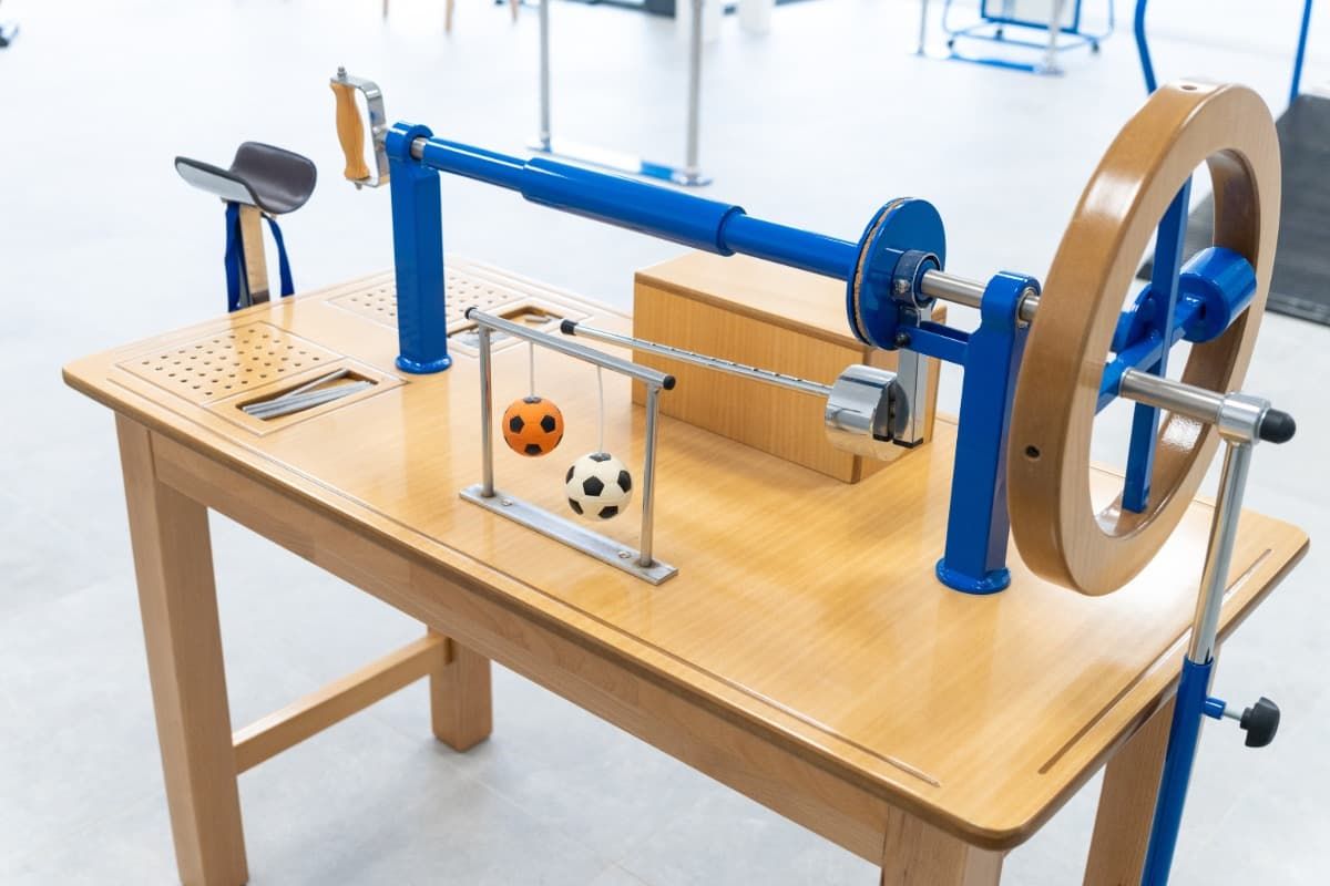Demostración de física en una mesa de madera con componentes metálicos de color azul y una rueca con bolas colgantes.