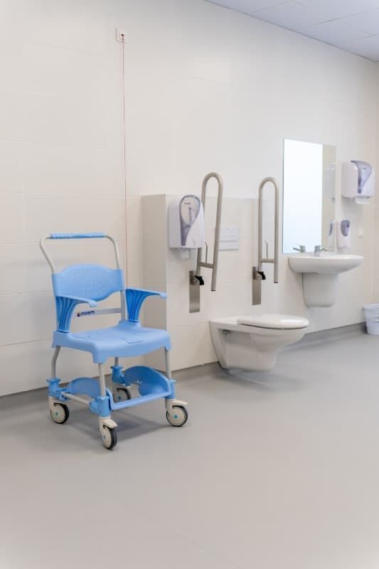 Silla de ducha médica azul en un baño de color claro con inodoro y lavabo.