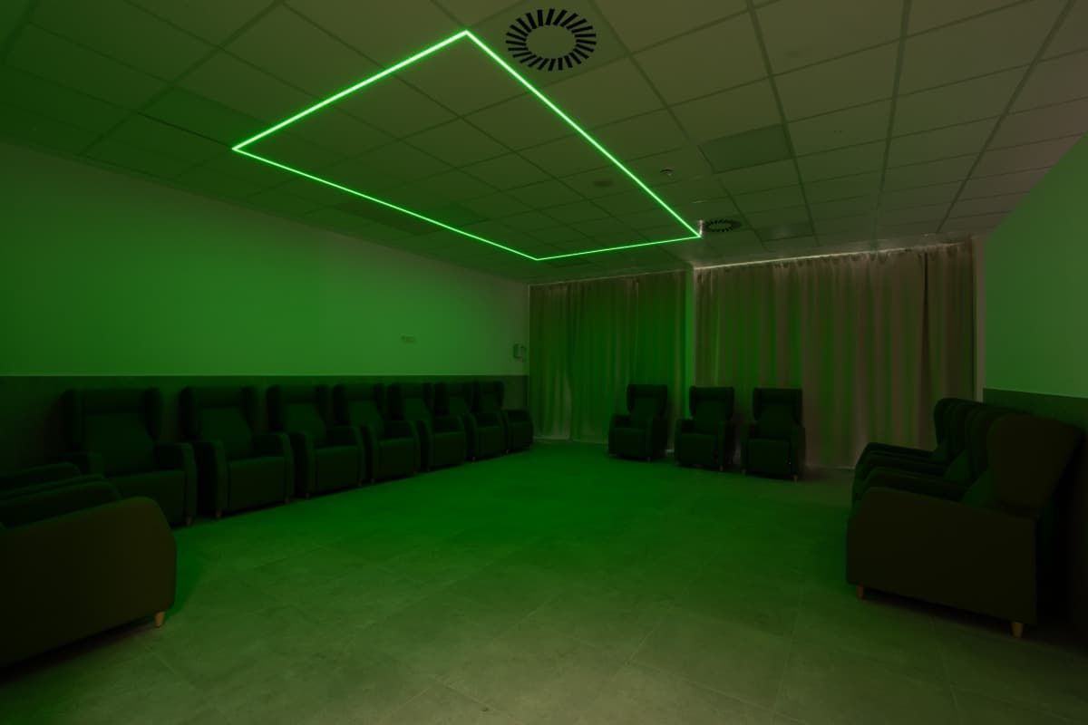 Una habitación iluminada con luz verde, lujosos asientos y una lámpara de techo geométrica.