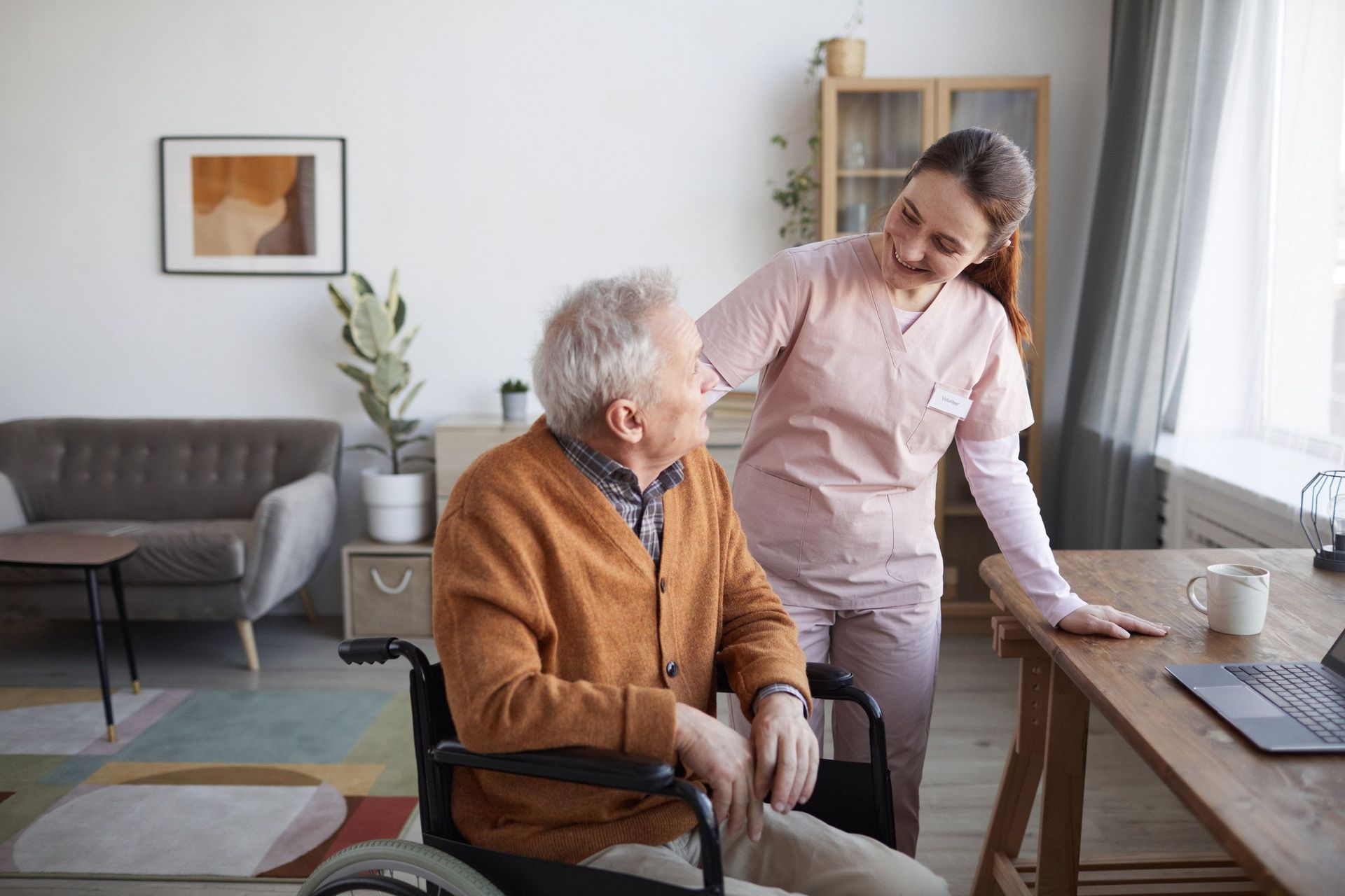 Una enfermera está ayudando a un anciano en silla de ruedas.