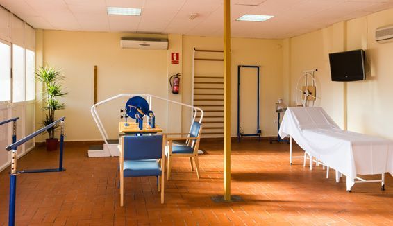 Una habitación con una cama, sillas y un televisor en la pared.