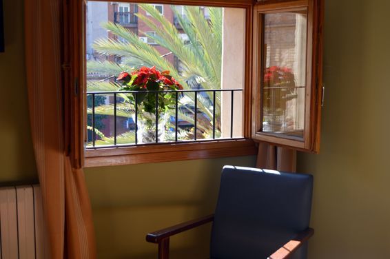 Una silla frente a una ventana con un jarrón de flores.