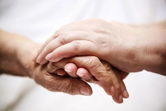 Una mujer sostiene la mano de una mujer mayor.