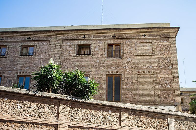 Un gran edificio de ladrillo con un muro de piedra delante.