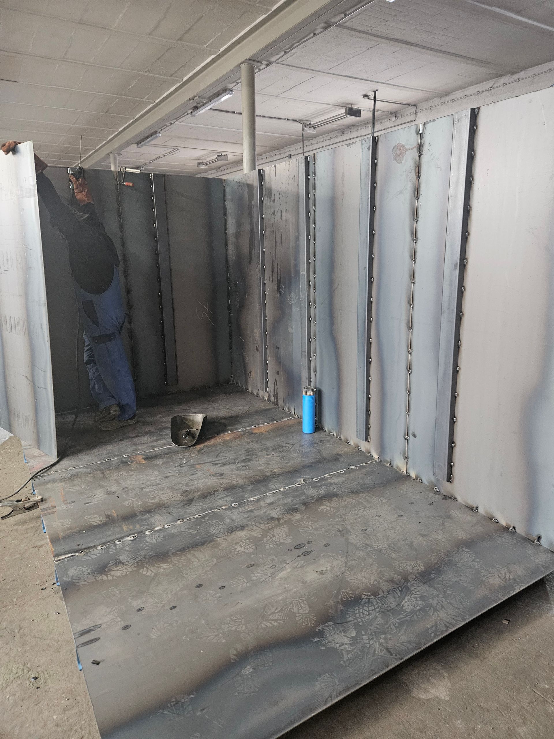 Im Innenbereich wird eine geschweißte Metallkonstruktion errichtet; Arbeiter in der Nähe.