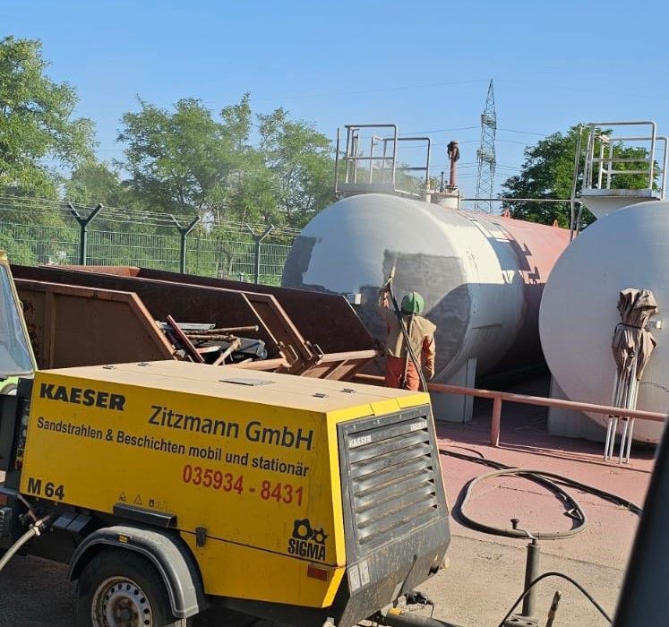 Gelber Kompressor und Tanks mit Arbeiter. Industriegelände; auf dem Kompressor steht „Kaeser“.