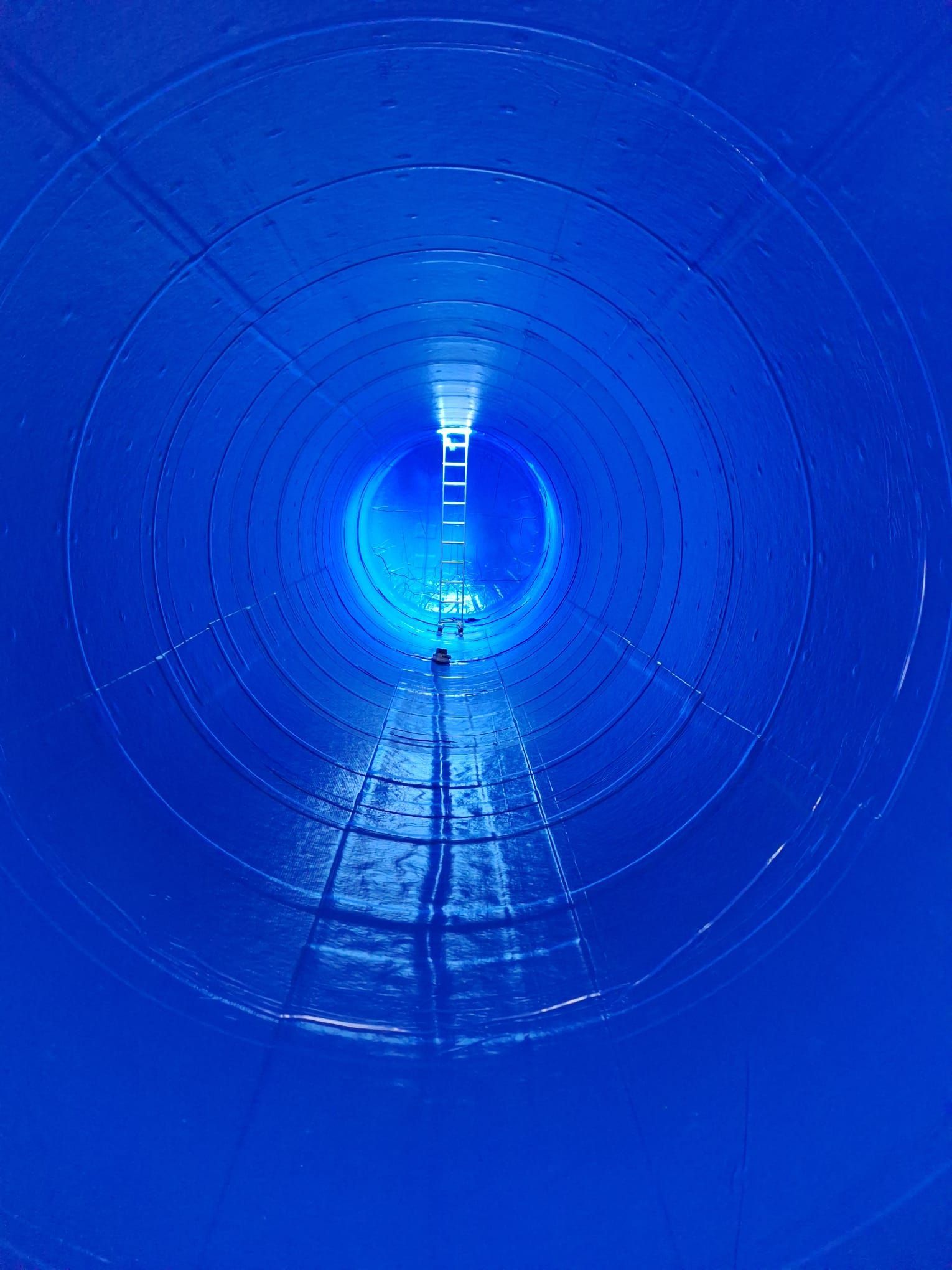 Im Inneren befindet sich eine große, blaue zylindrische Struktur, an deren Ende eine Leiter sichtbar ist.