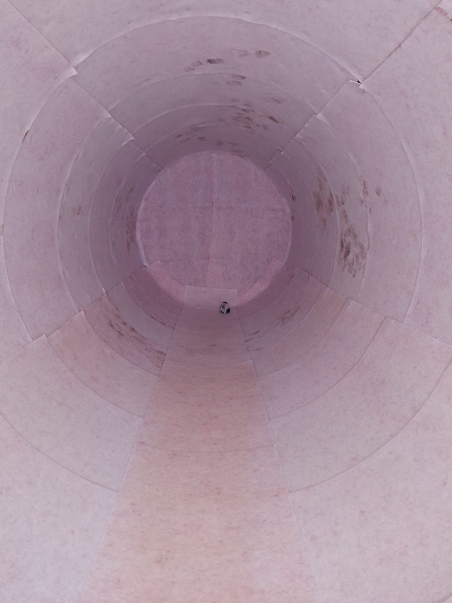 Blick nach oben in das Innere einer hohen, zylindrischen Struktur: Hellrosa Wände laufen in einem kleinen, dunklen Zentrum zusammen.