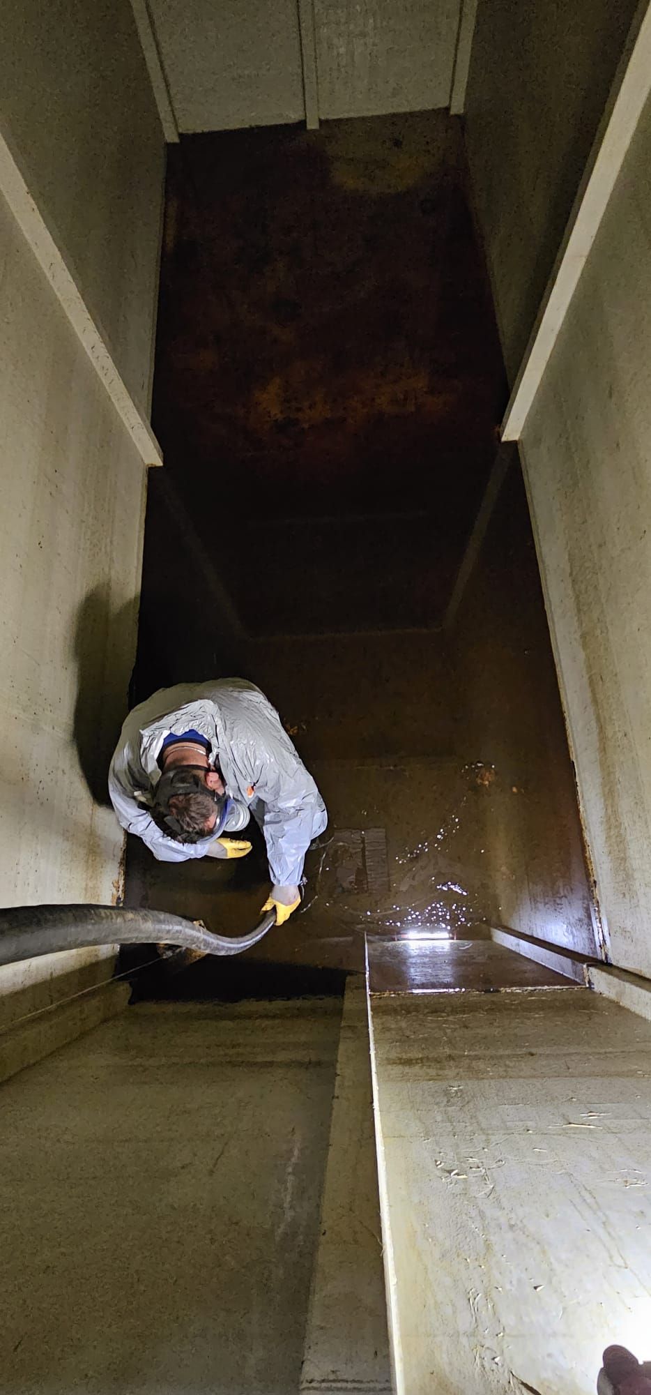 Person, die mit einem Schlauch und Licht das Innere einer Betonkonstruktion, wahrscheinlich eines Wassertanks oder Ähnlichem, reinigt.