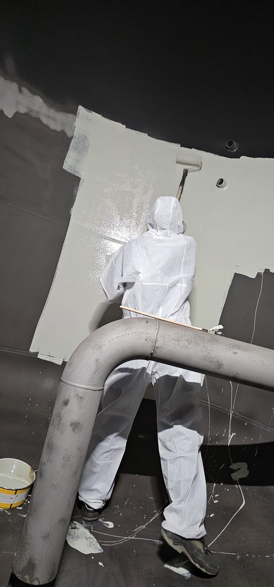 Eine Person im Schutzanzug streicht das Innere eines großen zylindrischen Tanks.