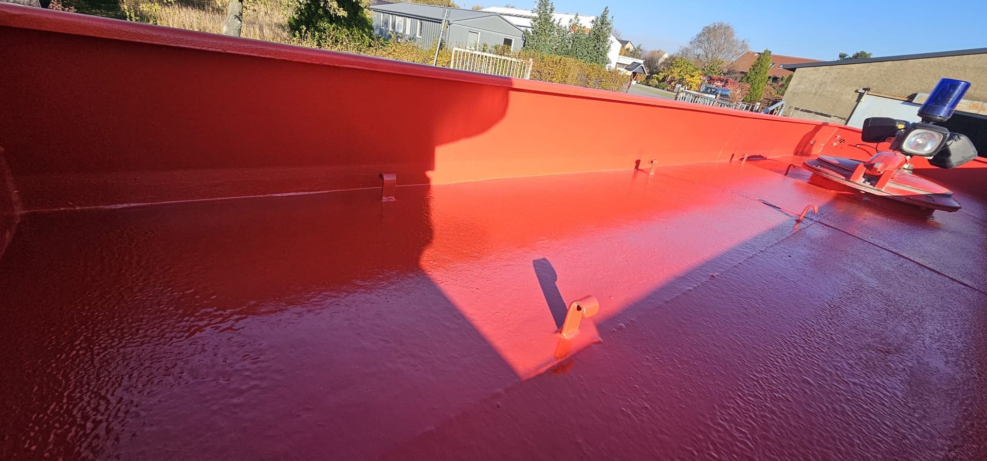 Leuchtend rotes Dach mit feuchter Versiegelung, im Hintergrund ein strahlend sonniger Himmel.