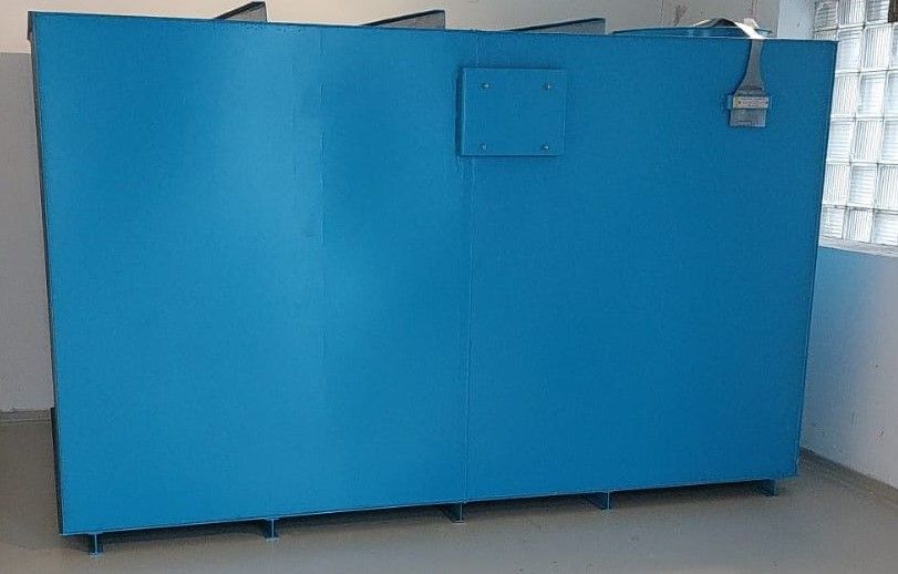 Großer, blauer, rechteckiger Wassertank mit Metallbeinen und einer quadratischen Zugangsklappe, im Innenbereich neben einem gemauerten Fenster.