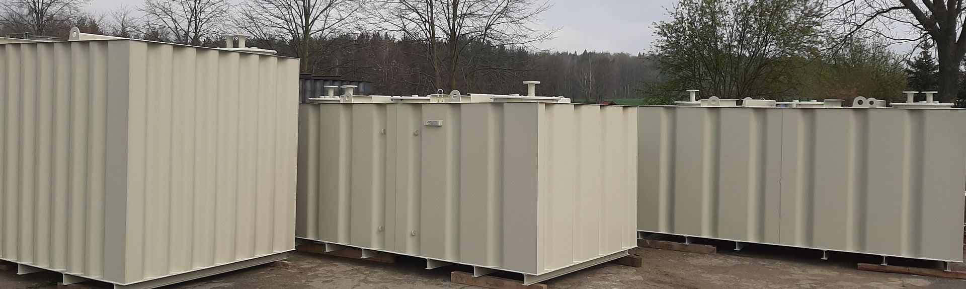 Drei beigefarbene Metalllagertanks sind draußen vor einer Baumgrenze aufgereiht.