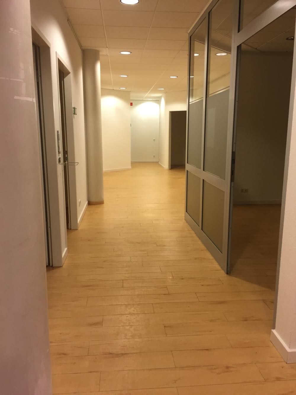 Ein langer Flur mit Holzboden und Glastüren in einem Bürogebäude.