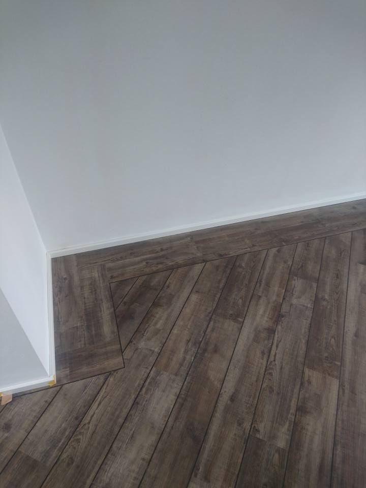 Eine Zimmerecke mit Holzboden und weißer Wand.