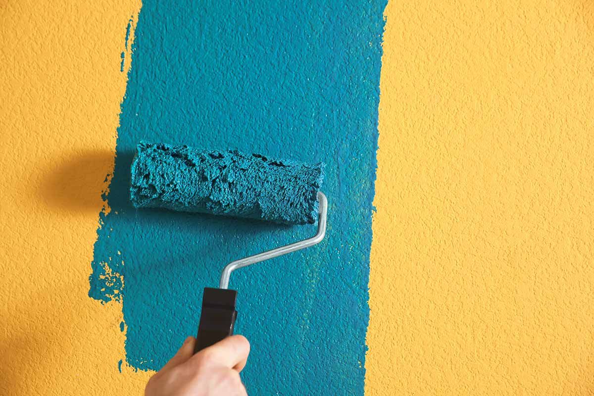 Una persona está pintando una pared amarilla con un rodillo de pintura azul.