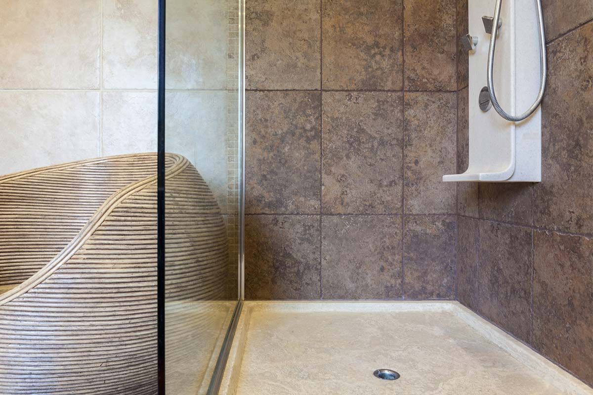 Un baño con ducha a ras de suelo y una silla de mimbre.