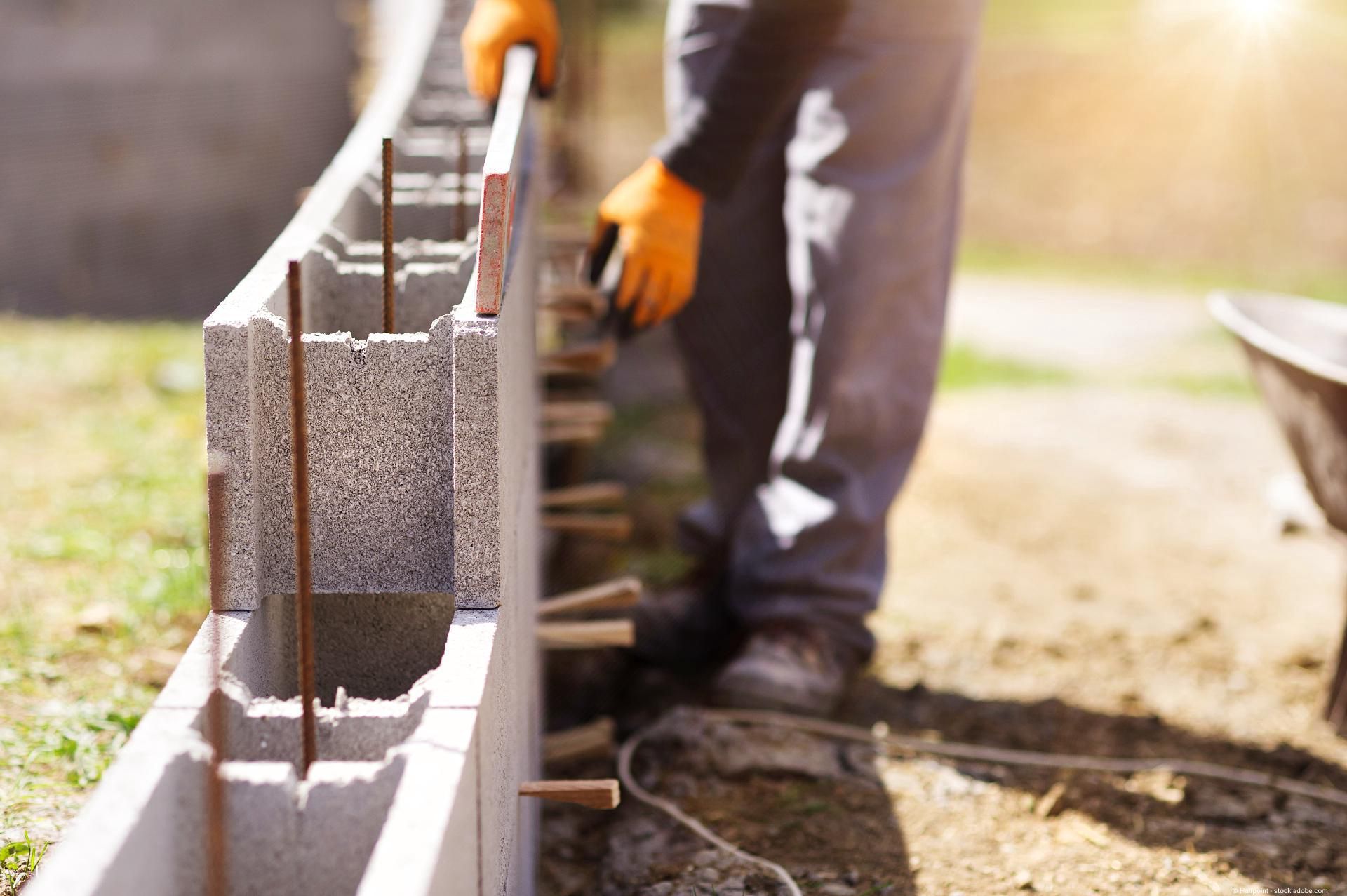 Bauarbeiter errichtet eine Mauer aus Betonsteinen mit Stahlbewehrung auf einer Baustelle.