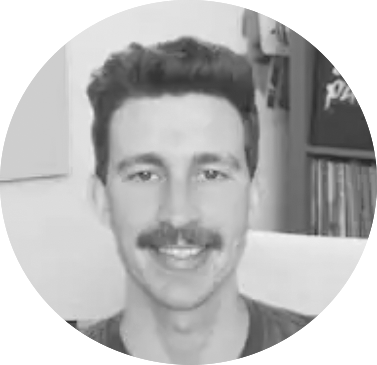 Grayscale headshot of a smiling man with dark hair and a mustache, indoors.