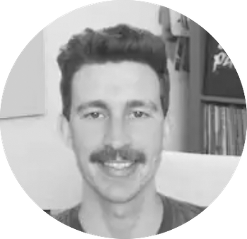 Grayscale headshot of a smiling man with dark hair and a mustache, indoors.