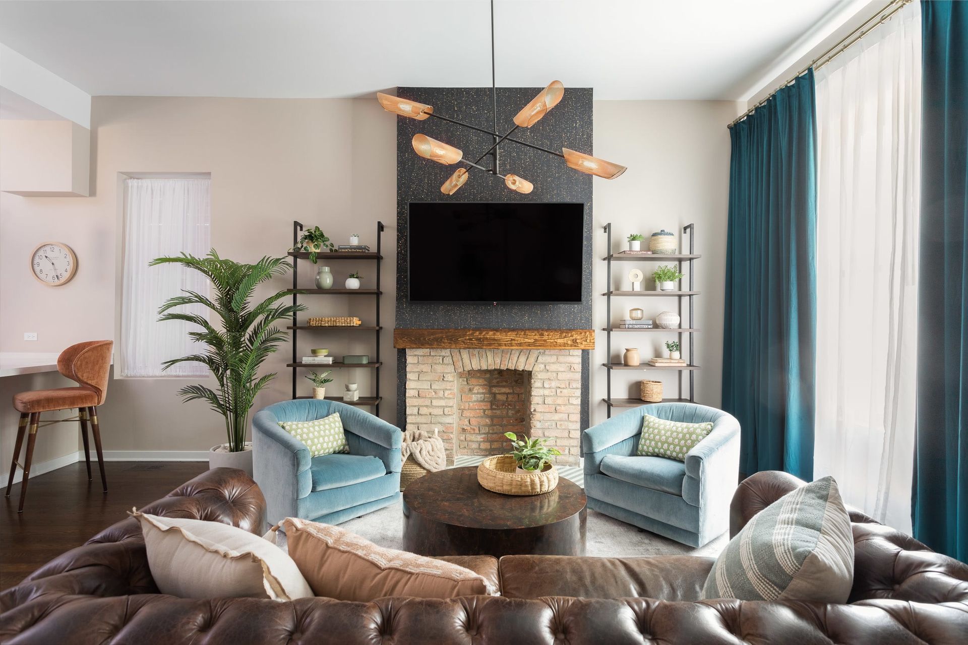 Bright living room with navy curtains, two blue chairs, a fireplace, and a wall-mounted TV with rustic decor