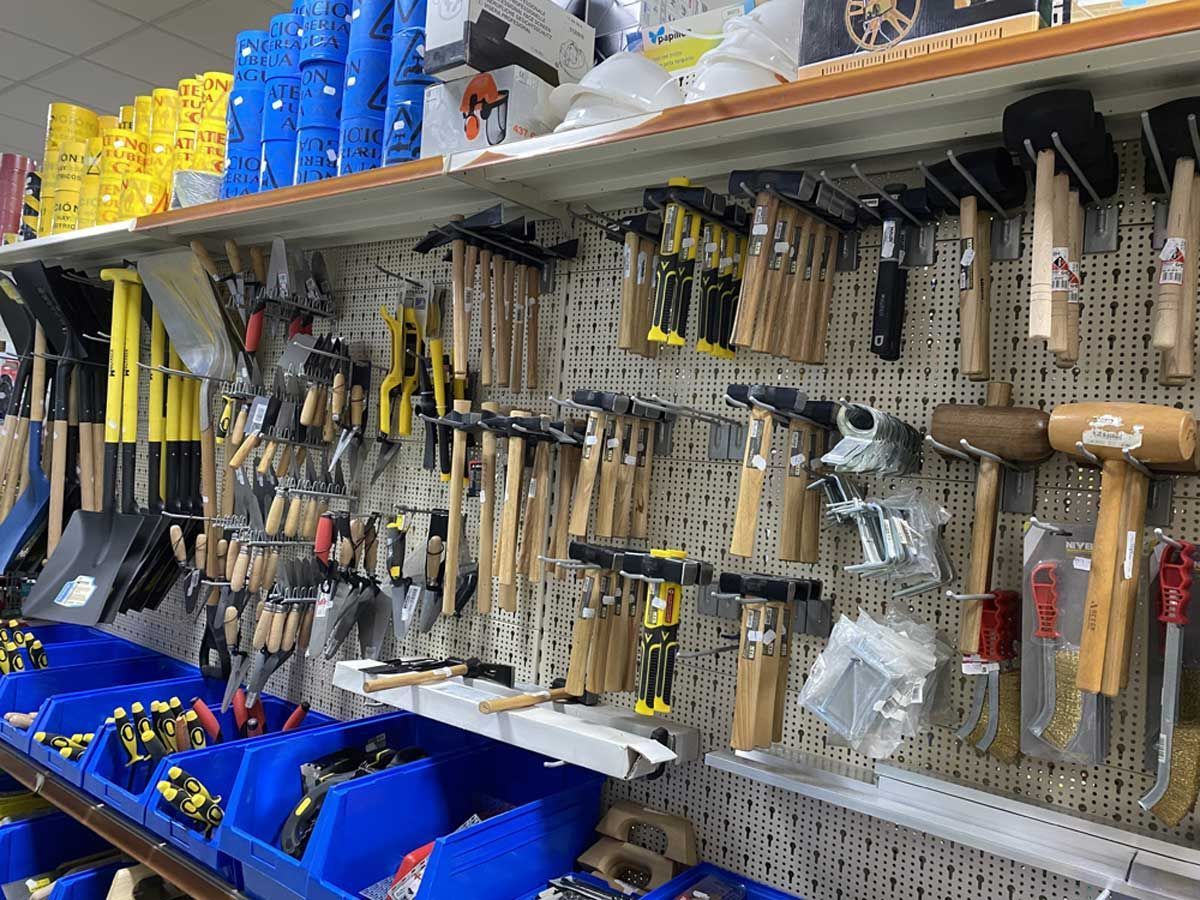 Un pasillo de una ferretería que exhibe diversas herramientas, entre ellas palas amarillas, martillos con mango de madera y contenedores de almacenamiento azules.