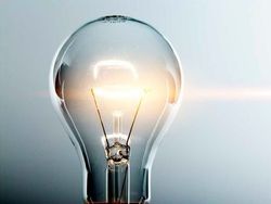 Una bombilla incandescente brillante y nítida centrada sobre un fondo azul claro y suave.